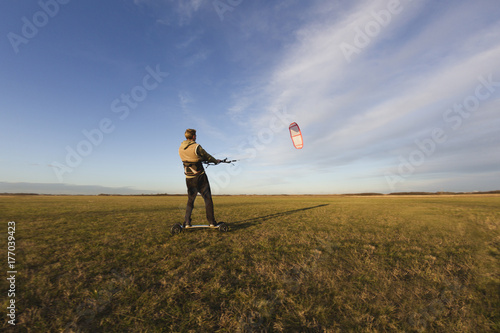 Young man kiteboarding in the field at sunset