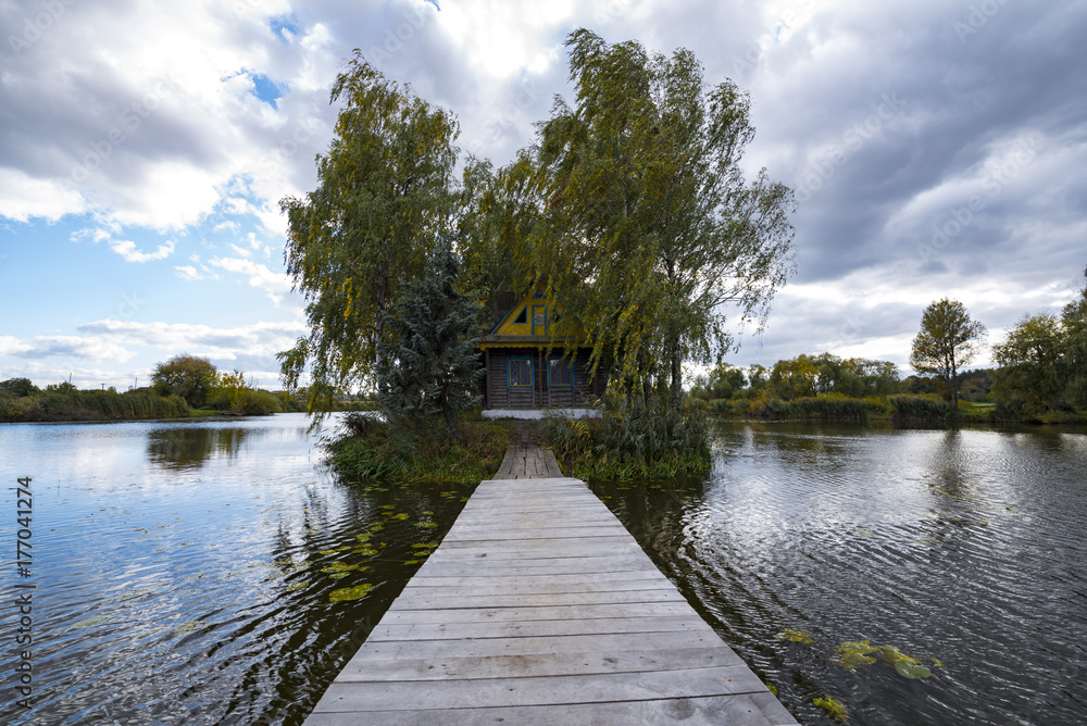 Lonely wooden house among lake with trees and bridge to the house Lonely wooden house among lake with trees and bridge to the house