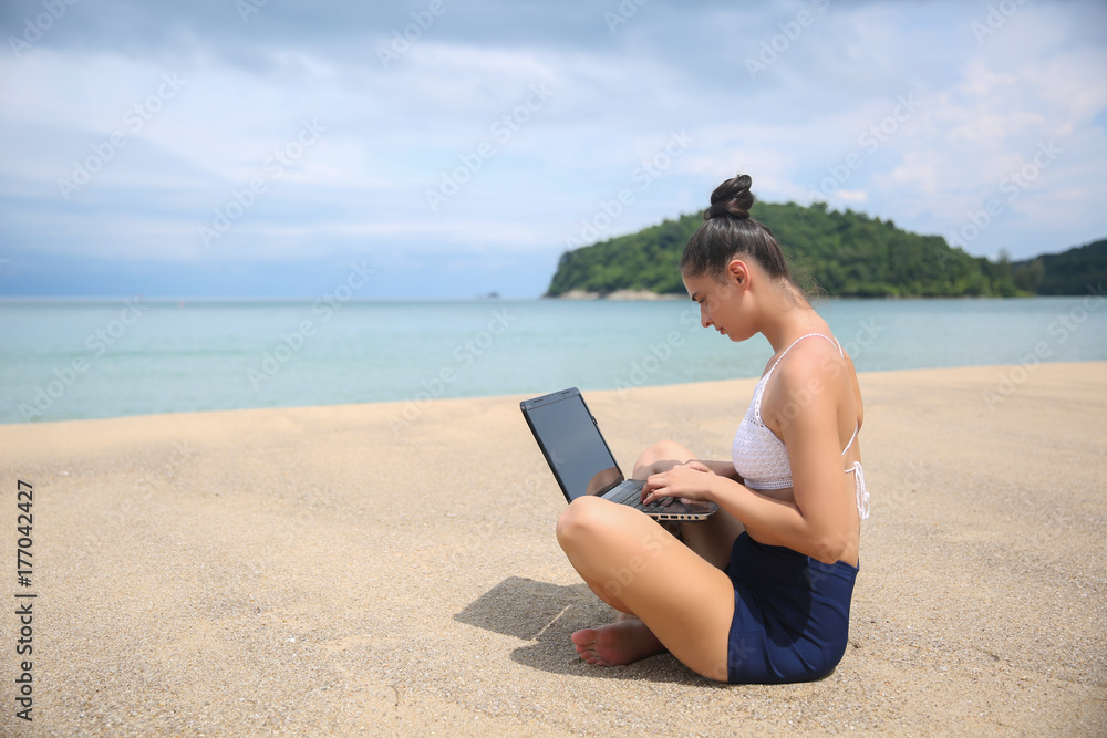 Young beautiful woman hipster traveler freelancer with laptop on the seashore. Business and vacation concept