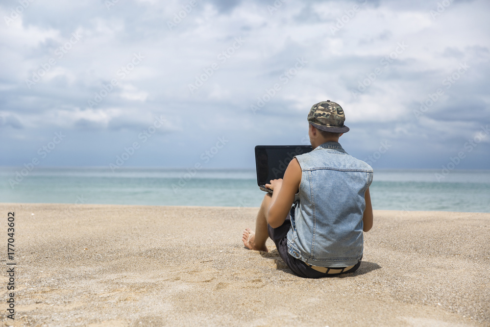 Young man working on laptop while sitting on the beach. Freelance working, social networks concept Young man working on laptop while sitting on the beach. Freelance working, social networks concept