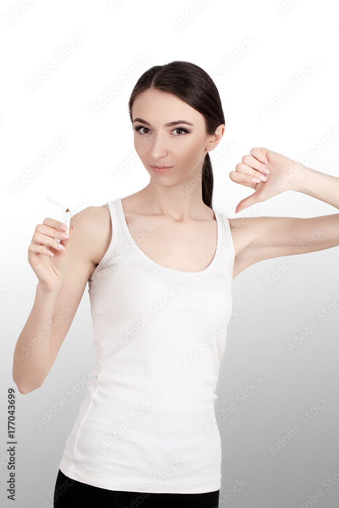 No smoking Portrait of a young woman with cigarettes in her arms. Humiliating sagayad. Caution against smoking. Lowers finger to bottom. On a gray background. No smoking Portrait of a young woman with cigarettes in her arms. Humiliating sagayad. Caution against smoking. Lowers finger to bottom. On a gray background.