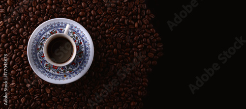traditional hot coffee cup with beans over a black background.