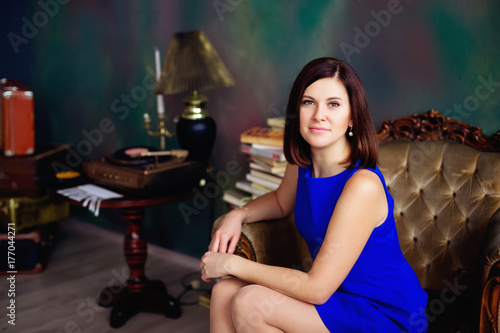 Brunette woman in blue short dress looks at camera sitting on ar