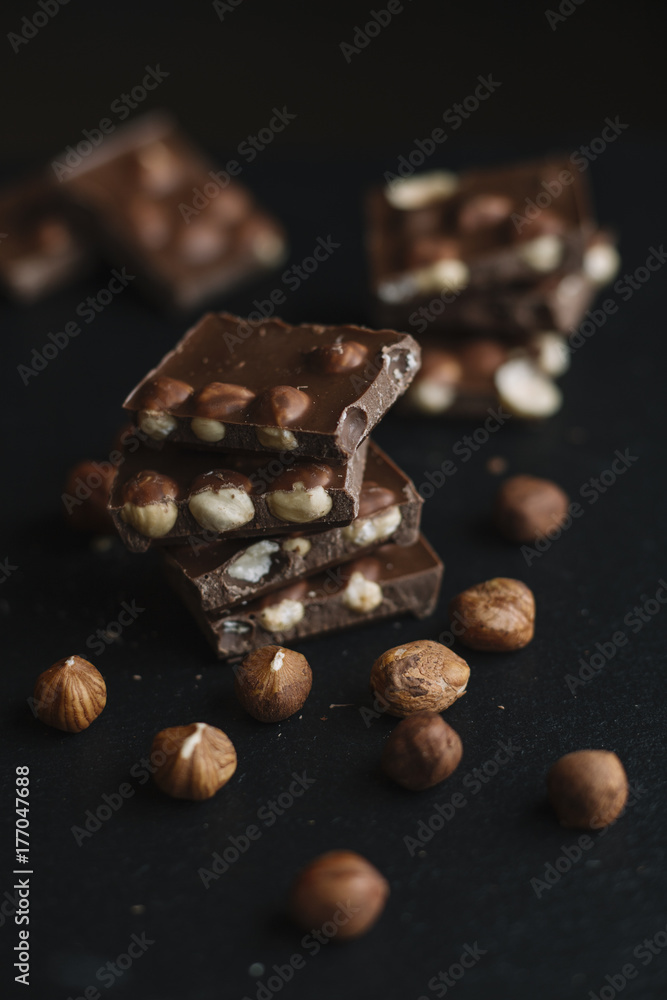 Chocolate bar pieces and nuts on dark slate background with copy space. Chocolate background. Top view. Toned Chocolate bar pieces and nuts on dark slate background with copy space. Chocolate background. Top view. Toned