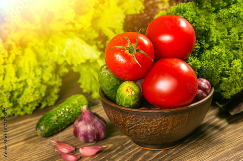 Tomatoes, garlic bulb and cucumbers on a wooden table. Green salad in the background. The concept of a healthy diet photo