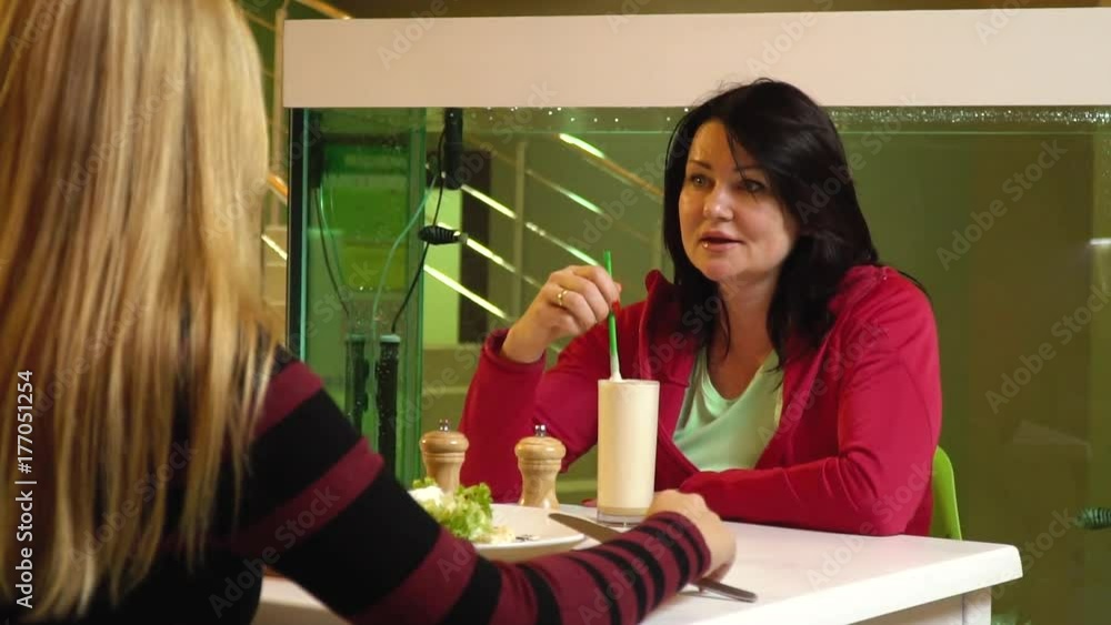 Two women sit near the aquarium in a cafe and chat, slow motion Two women sit near the aquarium in a cafe and chat, slow motion