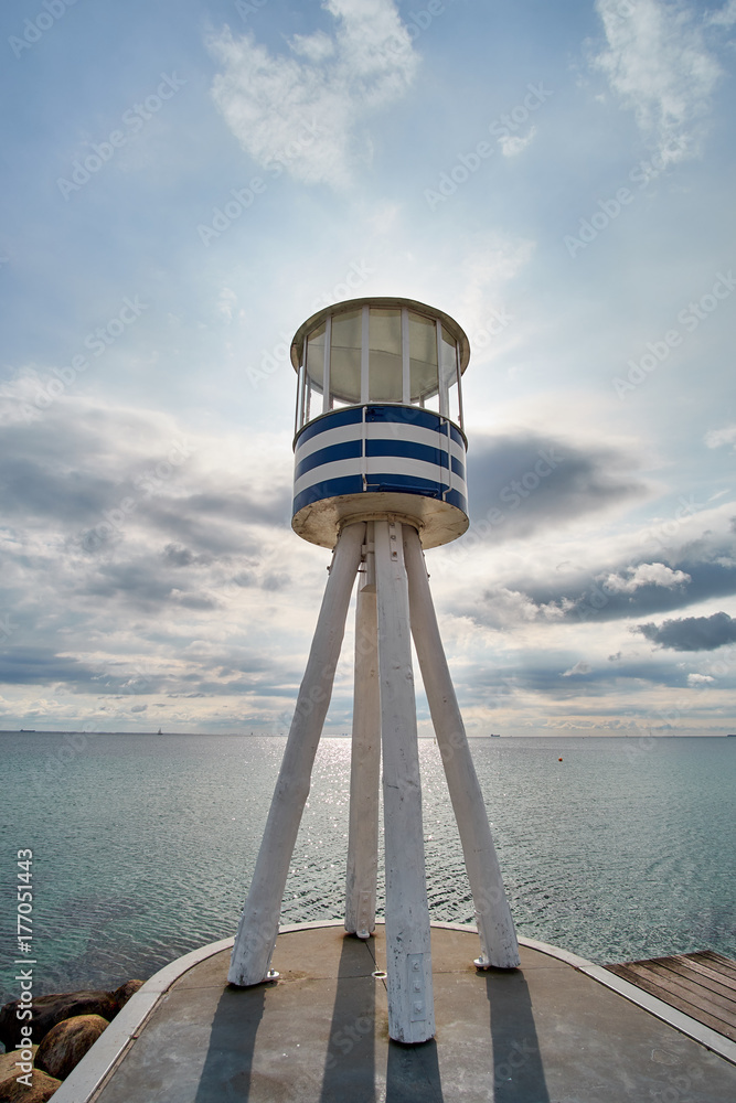 Low angle photography of a round barrel shaped life guard tower with blue and white stripes, standing on wood trunks