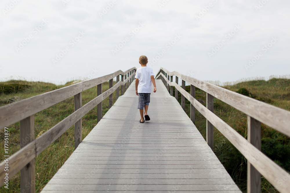 boy walking on a boardwalk toward the beach boy walking on a boardwalk toward the beach