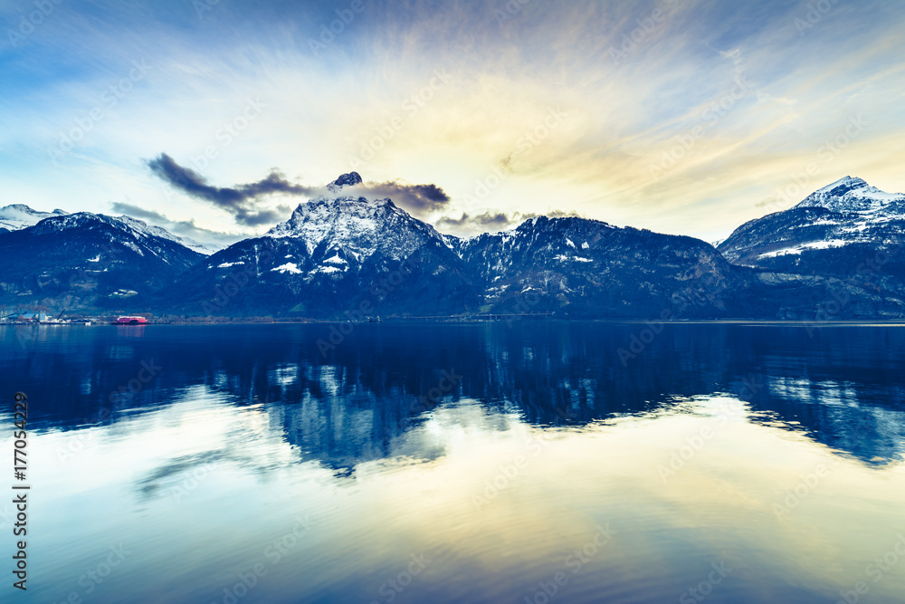 Bright sunset colors. Swiss Alps. Colorful sunset over the mountains and lake. Tops in the snow reflected in lake water.