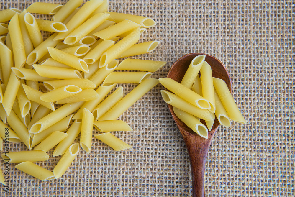 Penne raw pasta in wooden spoon on sack rustic background . Natural and healthy food concept. Penne raw pasta in wooden spoon on sack rustic background . Natural and healthy food concept.