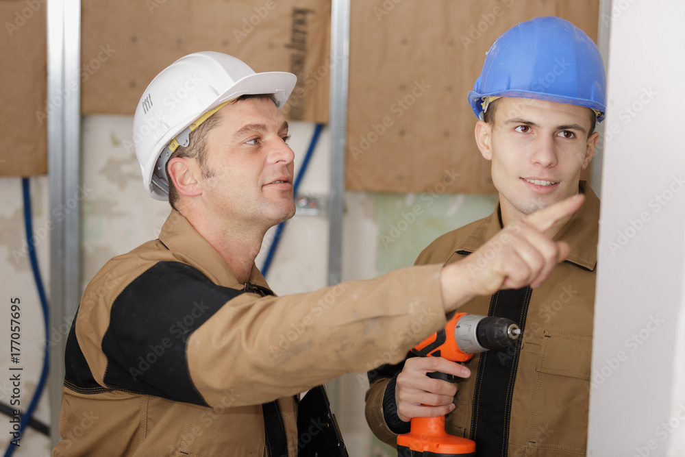 craftsman watching over his apprentice drill a wall craftsman watching over his apprentice drill a wall