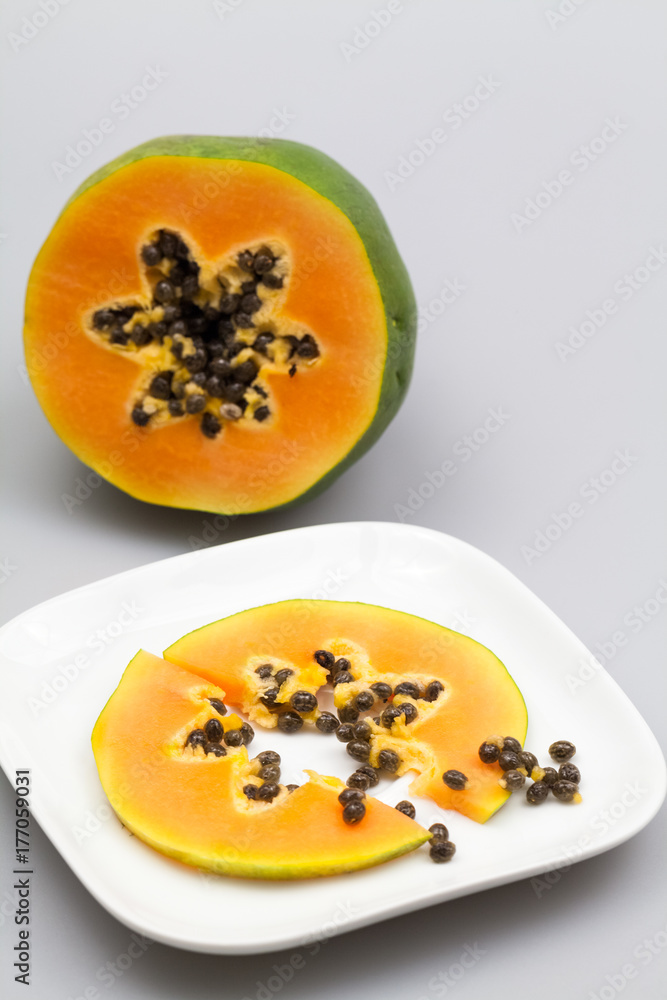 Papaya fruit - half and slice with seeds and light grey background
