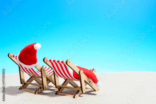Merry Christmas on beach concept. Two lounge chairs with Santa hats