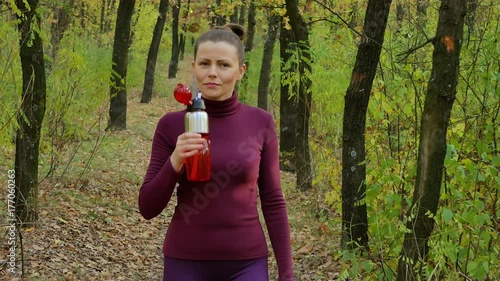 Beautiful fitness sport girl walking along the autumn park in sportswear with sports water bottle or isotonic drink in hand. photo