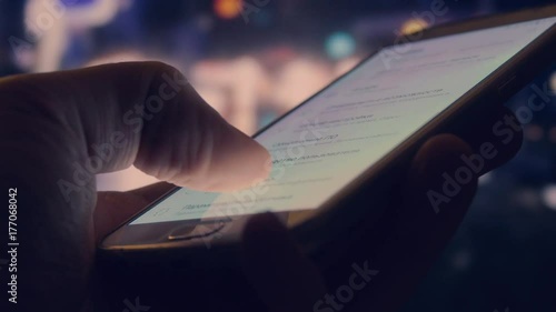 Man is using touching smartphone display outdoors. Blurred city night background photo