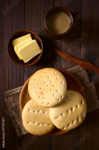 Traditional Chilean Hallulla bread rolls on wooden plate with butter and coffee with milk above, photographed overhead on dark wood with natural light photo