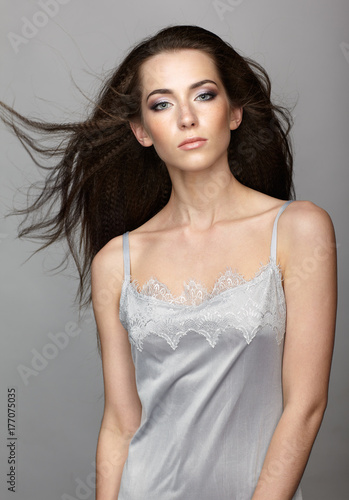 Beauty portrait of young woman. Brunette girl with long disheveled flying hair and day female makeup on gray background