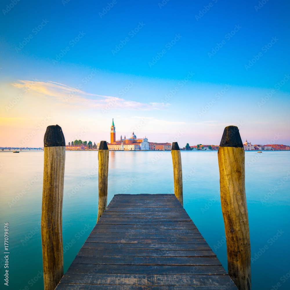 Venice lagoon, wooden pier or jetty and poles and church on background. Italy Venice lagoon, wooden pier or jetty and poles and church on background. Italy