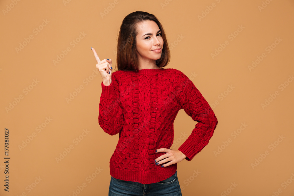 Close-up photo of charming brunette woman in red knitted sweater pointing with finger, looking at camera Close-up photo of charming brunette woman in red knitted sweater pointing with finger, looking at camera