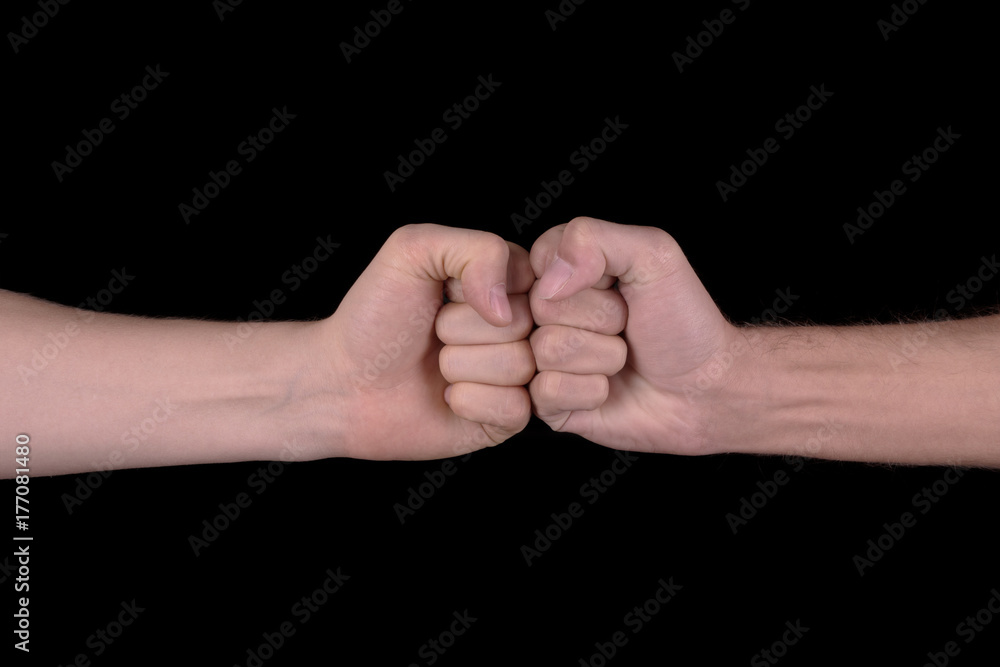 The image close-up of the collision of two fists on a black background. The concept of confrontation, competition or friendship The image close-up of the collision of two fists on a black background. The concept of confrontation, competition or friendship