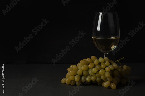 White wine in a glass with fall grapes, dark photo, dark background
