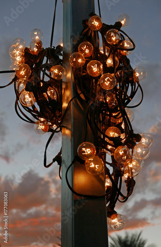 An einem Mast aufgewickelte Lichterkette mit Glühbirnen vor einem Abendhimmel mit roten Wolken © Dietlinde DuPlessis