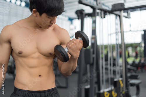 Fitness man in training showing exercises with dumbbells in gym