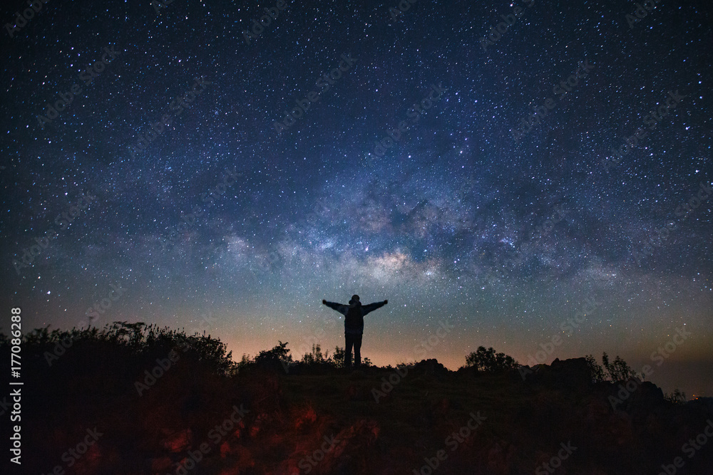 Landscape with milky way galaxy, Starry night sky with stars and silhouette of a standing sporty man with raised up arms on high mountain.