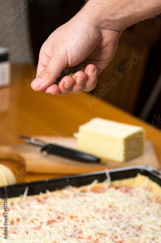 Man putting oregano on to pizza in making