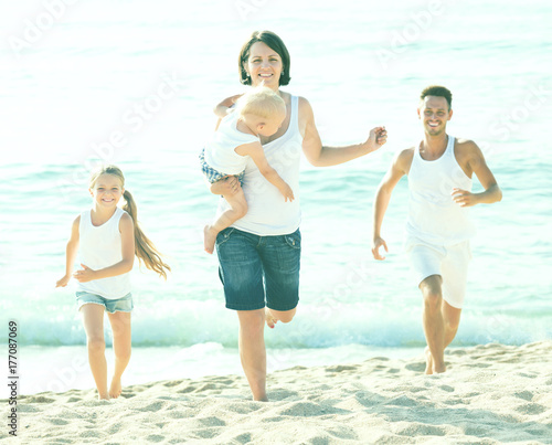 family of four running on sandy beach on sunny weather
