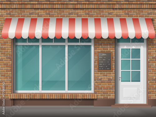 Cafe or store front with large transparent window and awning. Facade of red brick. Empty glass showcase of boutique. Entrance in the small  shop.