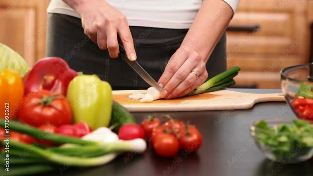 Woman hands chopping spring onion for a vegetables salad - side view of the cutting board at the kitchen table, camera slide Woman hands chopping spring onion for a vegetables salad - side view of the cutting board at the kitchen table, camera slide