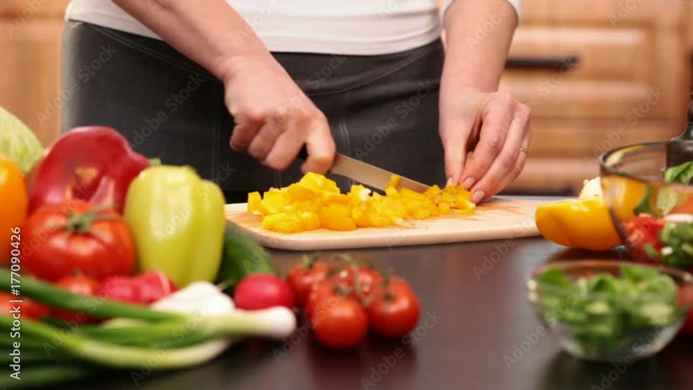 Woman hands chopping yellow pepper slices for a vegetables salad - side view of the cutting board at the kitchen table, camera slide Woman hands chopping yellow pepper slices for a vegetables salad - side view of the cutting board at the kitchen table, camera slide