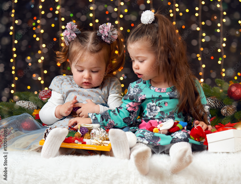 two girls unpack gifts in christmas decoration, dark background with illumination and boke lights, winter holiday concept