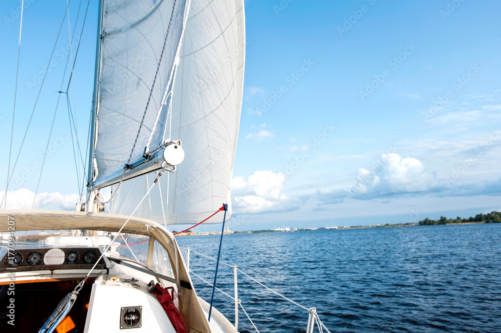 White yacht drifts in sunlight on blue cloudy sky background. White yacht drifts in sunlight on blue cloudy sky background.