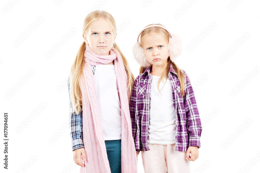 Portrait of two little sisters wearing scarf and earmuffs posing against white background Portrait of two little sisters wearing scarf and earmuffs posing against white background