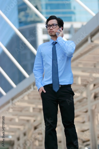 Soft focus young Asian business man talking on phone for his job at outdoor street background.