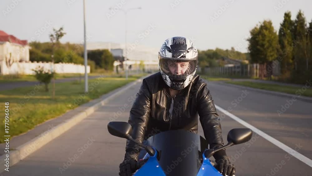 A motorcyclist rides a city on his yellow-blue motorcycle in a helmet and a leather jacket. Close-up A motorcyclist rides a city on his yellow-blue motorcycle in a helmet and a leather jacket. Close-up