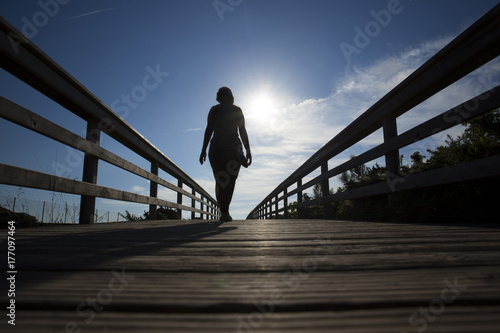 mujer pasando por un puente hacia el sol