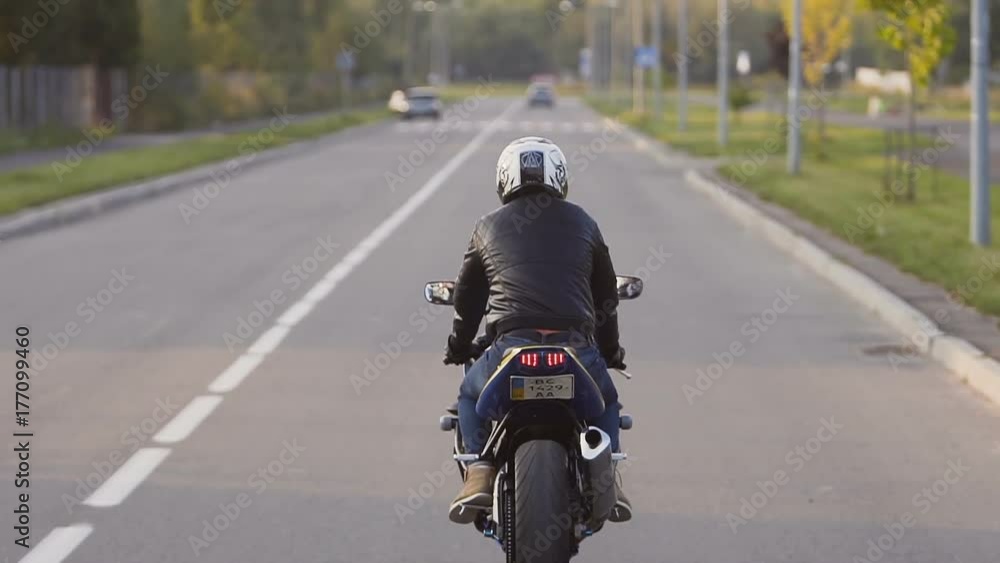 A young biker in a leather jacket and a helmet riding at the motorcycle along the highway around the city A young biker in a leather jacket and a helmet riding at the motorcycle along the highway around the city