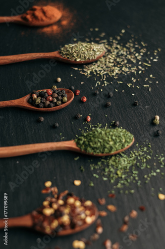 Close up of spices in wooden spoons on black slate board.