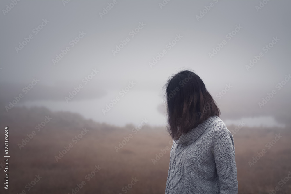 Depressive Frau steht am Wasser im Nebel