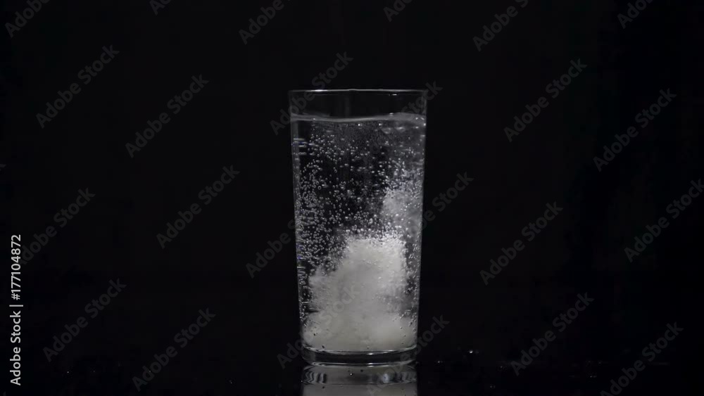 Effervescent tablet falling in a glass of water in slow motion on black background. Taking medication concept. Taking calcium, magnesium, vitamins, aspirin for a healthy life. Effervescent tablet falling in a glass of water in slow motion on black background. Taking medication concept. Taking calcium, magnesium, vitamins, aspirin for a healthy life.