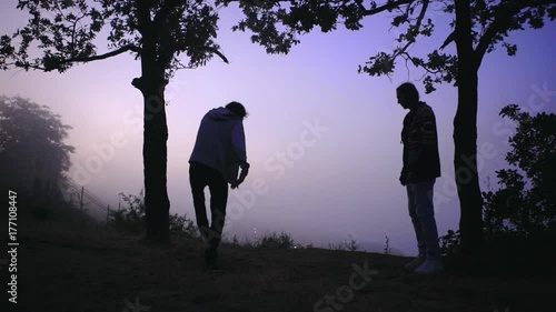 atmospheric picture of two tall slim men playing footbag freestyle early in morning on hill over sea covered with fog in slow motion photo