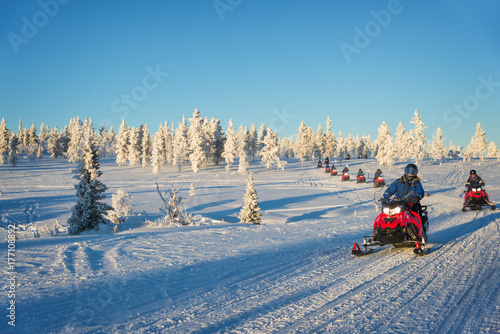 Group of tourists riding snowmobiles in a snowy winter landscape in Lapland, near Saariselka, Finland. Winter holiday sports and adventure in Scandinavia