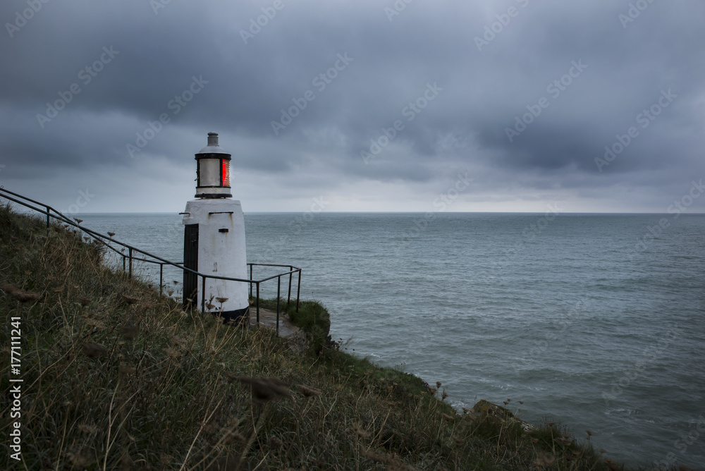 Lighthouse shining its red beacon on a gloomy day , Polperro, Cornwall, UK