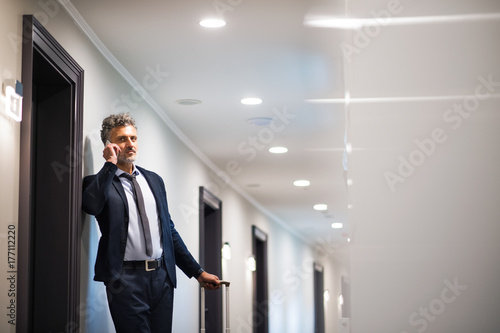 Mature businessman with smartphone in a hotel corridor.
