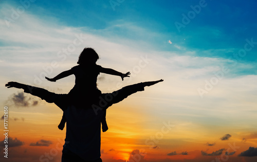 father and little daughter play at sunset sky