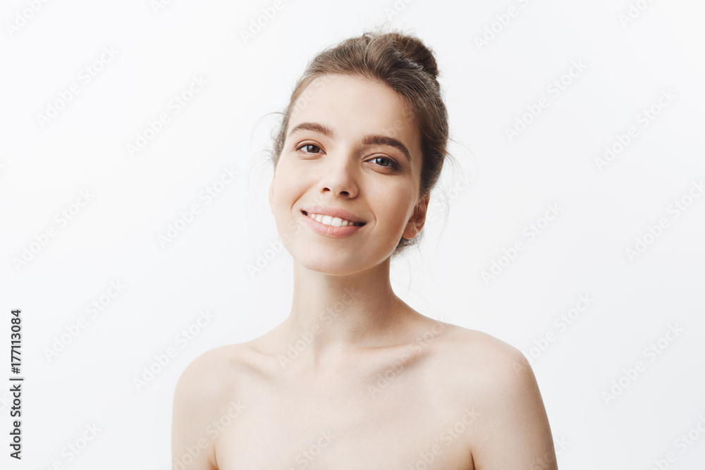 Cheerful beautiful young mother with long dark hair in bun hairdo being naked smiling brightfully in camera, being happy about her motherhood. Young family concept