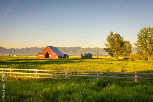 Fotografia Summer sunset with a red barn in rural Montana and Rocky Mountains